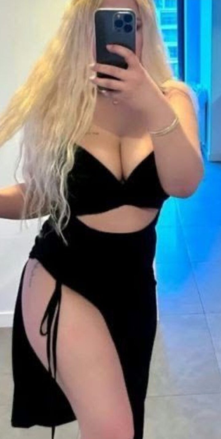 Woman taking a mirror selfie in a black crop top/bandeau with a high-slit skirt.