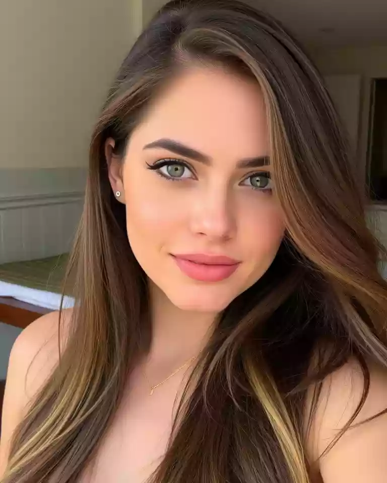 Close-up portrait of a young woman with long brown hair, green eyes, and pink lips looking at the camera. In natural light with a soft smile.