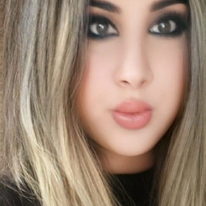 Close-up of a woman with long blonde hair, smoky eye makeup, and nude pink lips, looking at the camera.